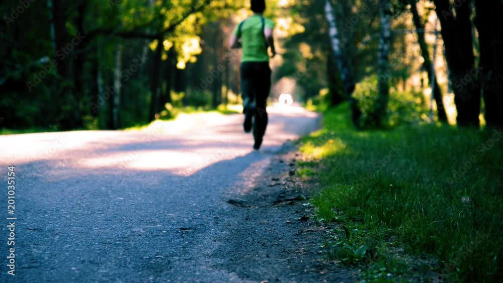 FHD sport man running at new asphalt road outdoor. Sunrise or sunset in rural city park. Green tree forest and sun rays on horizon. FHD sport man running at new asphalt road outdoor. Sunrise or sunset in rural city park. Green tree forest and sun rays on horizon.