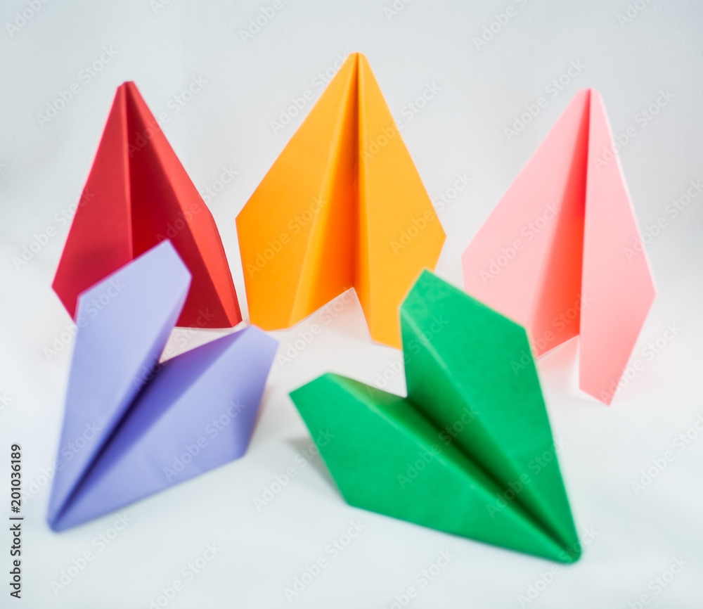 Colorful paper planes. Red paper plane among green, blue, peachy, and yellow ones on a white background, isolated. Concept (idea) of airlines, freedom, leadership, success, and individualism. Colorful paper planes. Red paper plane among green, blue, peachy, and yellow ones on a white background, isolated. Concept (idea) of airlines, freedom, leadership, success, and individualism.