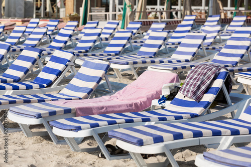 chaise lounges with blue mattresses stand on the sand on the beach, one chaise longue is occupied