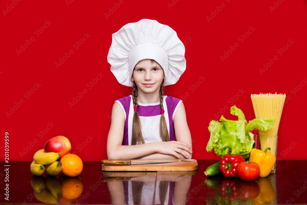 Happy little girl in chef uniform cuts fruit in kitchen. Kid chef. Cooking Process Concept Happy little girl in chef uniform cuts fruit in kitchen. Kid chef. Cooking Process Concept