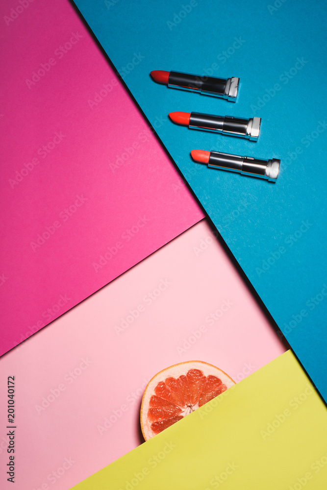 top view of various lipsticks with orange sllice on colorful surfaces