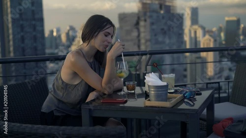 Pensive, young woman drinking cocktail in skybar 
 photo