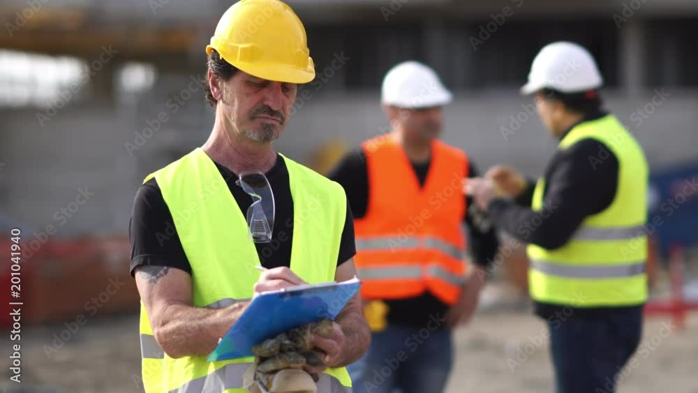 Absorbed civil engineer with protective workwear checking office blueprints on construction site Absorbed civil engineer with protective workwear checking office blueprints on construction site