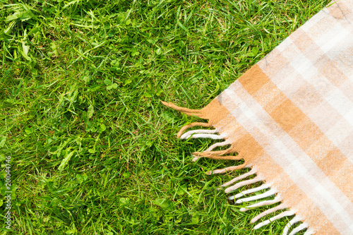 Green grass and checkered beige tablecloth background for picnic, top view