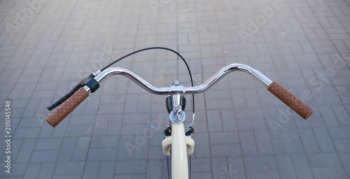 Steering wheel of a beige bicycle with brown handles on an avenue of paving slab