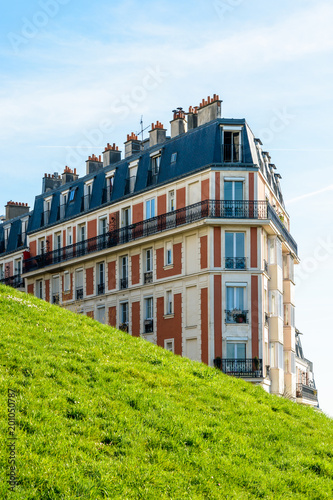 A 19th century parisian brick apartment building with a grassy slope in the foreground.