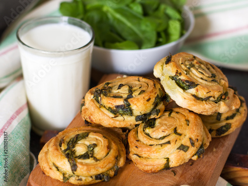 Buns of puff pastry with spinach and garlic on a wooden board in the background of a bowl of spinach and towels. Homemade pastries with greens.