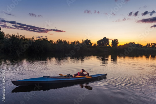 sporty man kayaking on river surrounded by forest at sunset