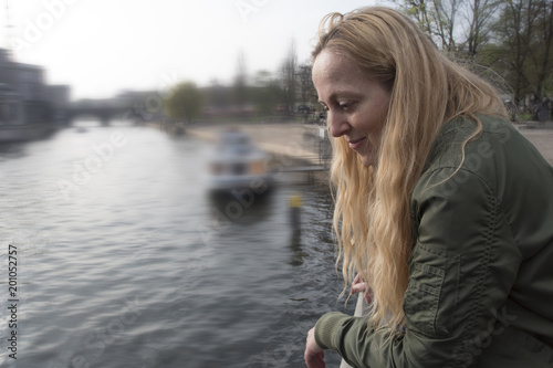 Mujer contenta mirando hacia abajo sobre a un canal con un barco al fondo.