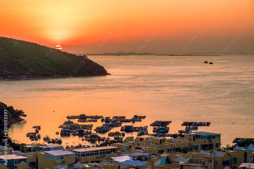 Small floating fishing farm in bay and village houses on the coastline. Beautiful lanscape background at tropical sunset golden hour. South East Asia, China, Hong Kong