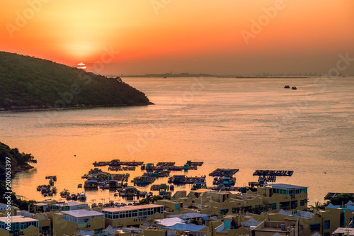 Small floating fishing farm in bay and village houses on the coastline. Beautiful lanscape background at tropical sunset golden hour. South East Asia, China, Hong Kong