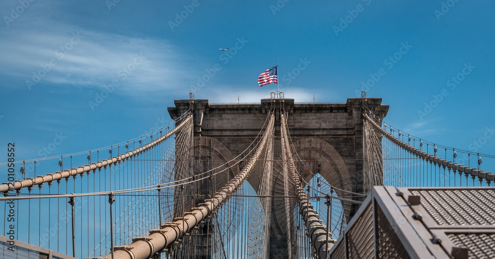 Fototapeta premium Brooklyn Bridge, New York, Manhattan with US flag and airplane at blue sky. panorama
