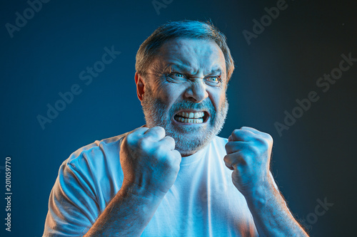 The senior emotional angry man screaming on blue studio background