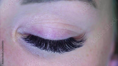 Extreme close up woman eye. Eyelash extension procedure. Cosmetologist combing eyelashes with a brush