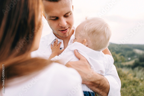 Walk of beautiful young family in white clothes with a young son blond in mountainous areas with tall grass at sunset. Dads carries his son on his shoulders. family - this is happiness