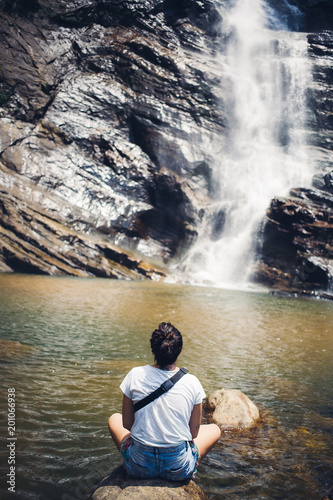 Woman seat before beautiful waterfall in Sri Lanka.