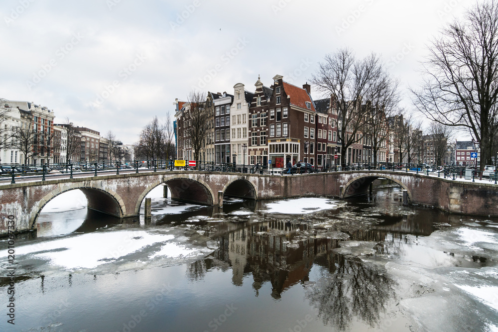 Naklejka premium Stunning view of Amsterdam canal frozen with snow during the cold wave in February 2018 on a very cold winter day.