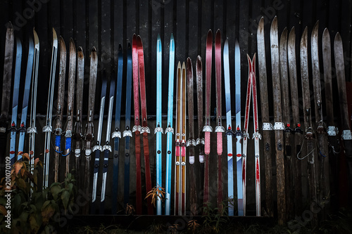 Red, blue, violet, black old ski made of wooden material with antique texture and grunge surface lean against the wooden dark wall of the house in northern Finland in Lapland in gloomy atmosphere