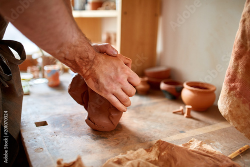 Hands of male potter molding a clay in pottery workshop, close-up, selective focus photo