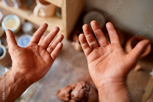 Mature male potter showing his palms while molding a clay in pottery workshop, close-up, selective focus photo