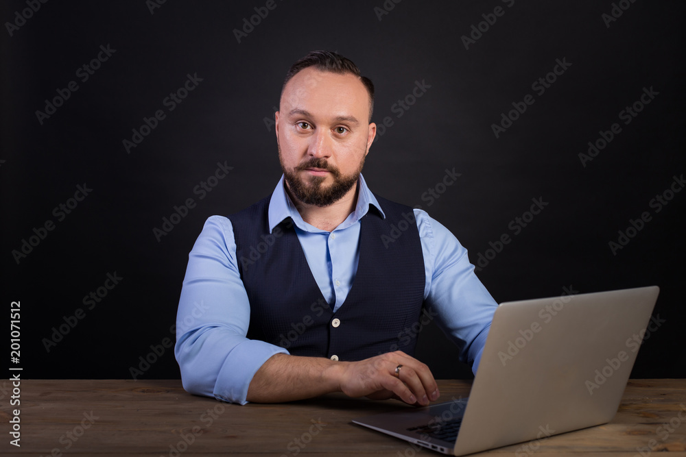Portrait of a confident businessman with laptop computer. Confident business expert. Young handsome man in shirt and waistcoat holding a laptop and smiling while standing against. Black background Portrait of a confident businessman with laptop computer. Confident business expert. Young handsome man in shirt and waistcoat holding a laptop and smiling while standing against. Black background