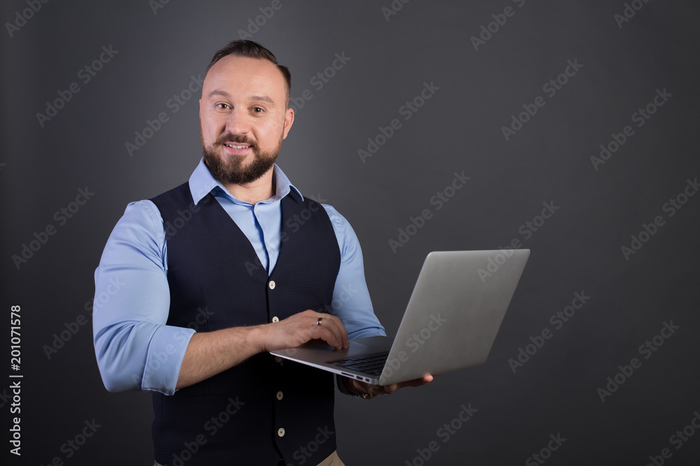 Portrait of a confident businessman with laptop computer. Confident business expert. Young handsome man in shirt and waistcoat holding a laptop and smiling while standing against. Black background Portrait of a confident businessman with laptop computer. Confident business expert. Young handsome man in shirt and waistcoat holding a laptop and smiling while standing against. Black background
