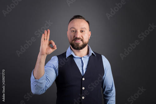 Happy young businessman showing ok sign over black background. Bearded businessman standing makes an okay gesture. Excited happy successful man showing sign ok.