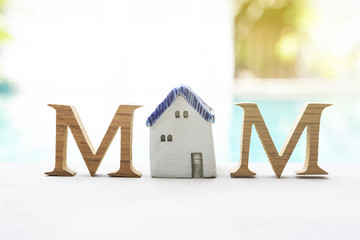 Mother's day concept, Wooden M text with vintage style ceramic house over blurred swimming pool background, outdoor day light