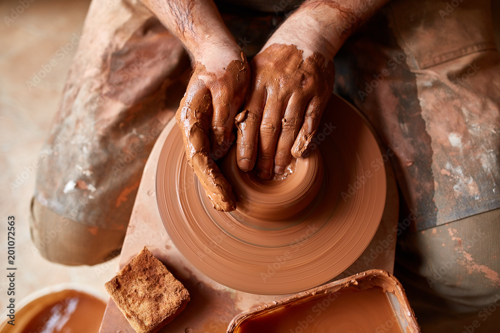 Close-up hands of a male potter in apron molds bowl from clay, selective focus