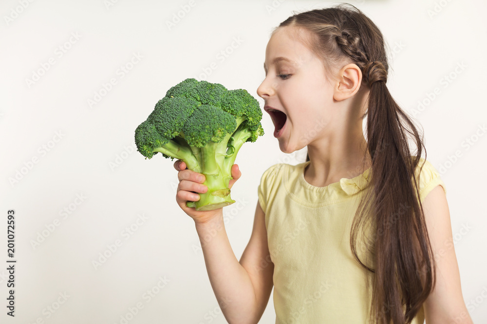 Pretty cute little girl biting broccoli over white background Pretty cute little girl biting broccoli over white background