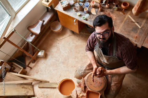 Portrait of a male potter in apron molds bowl from clay, selective focus, close-up photo