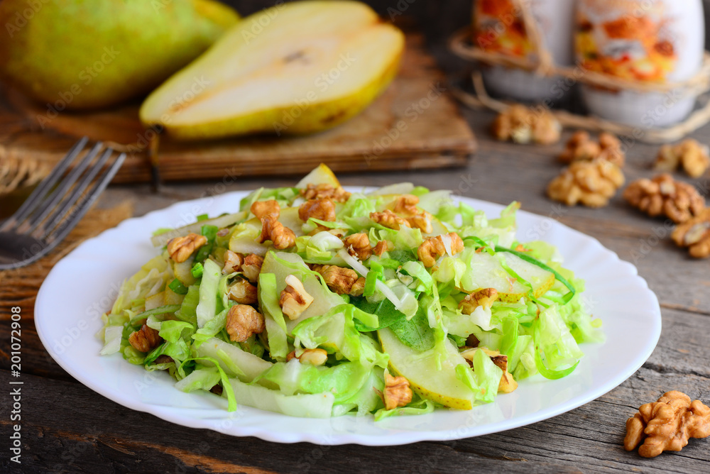 Quick pear and cabbage salad. Homemade salad with fresh pear, cabbage and walnuts on a white plate and on rustic wooden background. Quick healthy salad idea. Closeup Quick pear and cabbage salad. Homemade salad with fresh pear, cabbage and walnuts on a white plate and on rustic wooden background. Quick healthy salad idea. Closeup