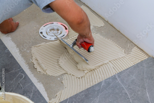 Troweling mortar onto a concrete floor in preparation for floor tile.