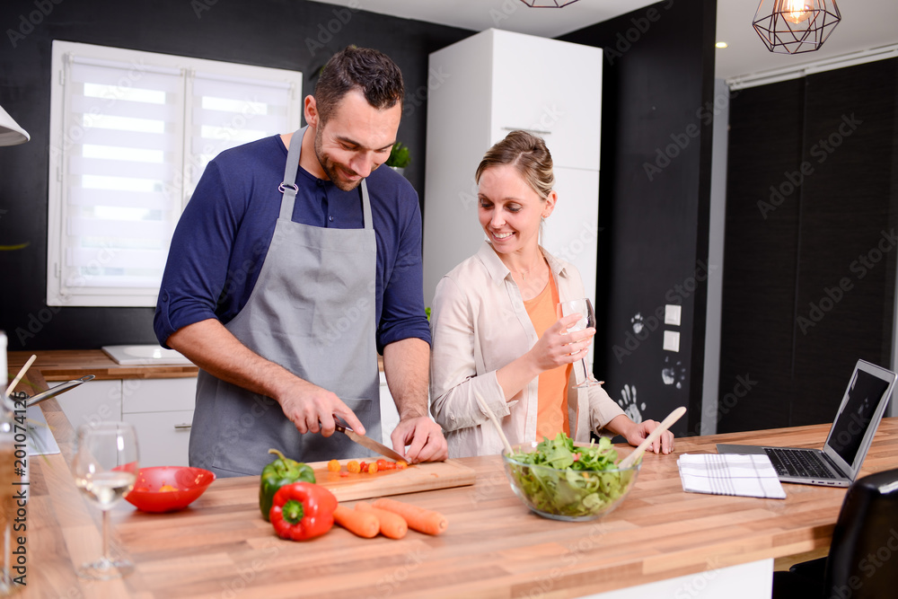 happy and cheerful young couple cooking organic vegetables together at home
