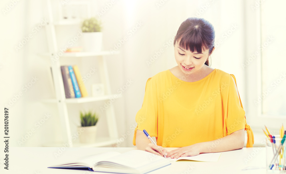 people, education, high school and learning concept - happy asian young woman student with book and notepad writing at home people, education, high school and learning concept - happy asian young woman student with book and notepad writing at home