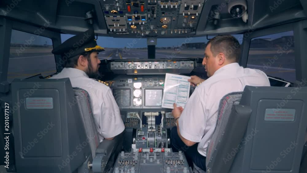 Pilots read a manual in a cockpit of a flight simulator. 4K.
