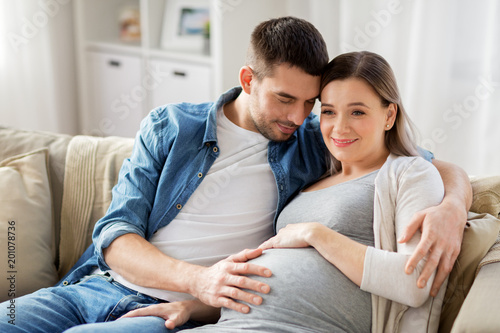 pregnancy and people concept - happy man hugging pregnant woman at home