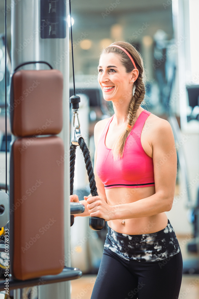 Happy and beautiful fit woman wearing pink fitness bra while exercising  cable rope triceps extension at the gym Stock Photo