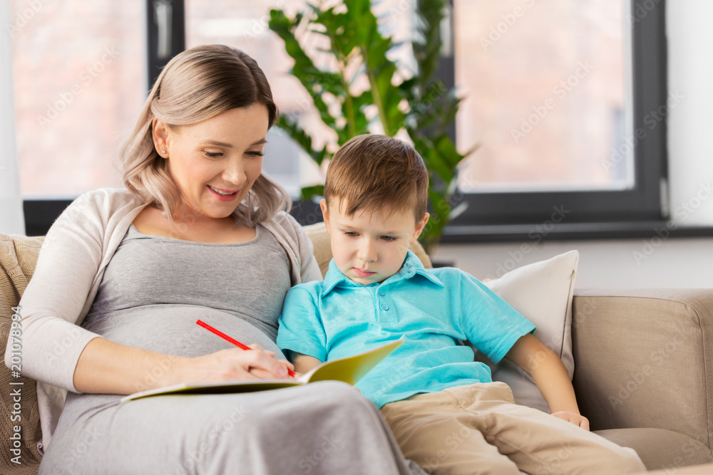 family, education and pregnancy concept - happy pregnant mother with little son writing or drawing in workbook at home family, education and pregnancy concept - happy pregnant mother with little son writing or drawing in workbook at home