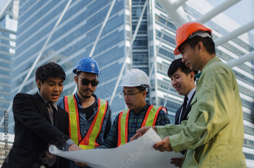 group of engineer, business man and architect with safety helmet planning about building plan with blueprint in modern city building background, construction site, business, industry, worker concept