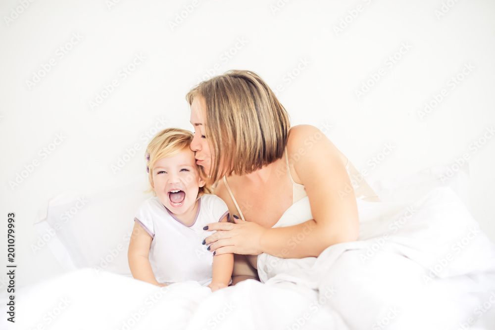 Happy and loving mother having fun and kissing her daughter on the bed. Family morning concept. Spending free time together at home. Soft selective focus. Space for text. Happy and loving mother having fun and kissing her daughter on the bed. Family morning concept. Spending free time together at home. Soft selective focus. Space for text.