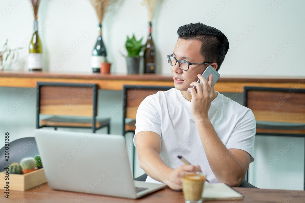 casual asian man talking on mobile phone working with laptop computer on wood table in coffee shop,Modern Digital lifestyle concept.influencer blogger review. casual asian man talking on mobile phone working with laptop computer on wood table in coffee shop,Modern Digital lifestyle concept.influencer blogger review.