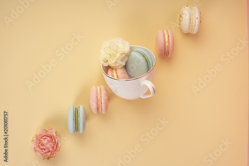 Multicolored macaroons cake are placed in a cup along with buds flowers while others are laid diagonally on  yellow background photo