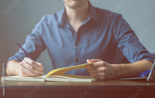 Close up of the hands of a businessman in a blue shirt signing or writing a document on a sheet of notebook. businessman or student writes information from portable prepare for lectures, Vintage color photo