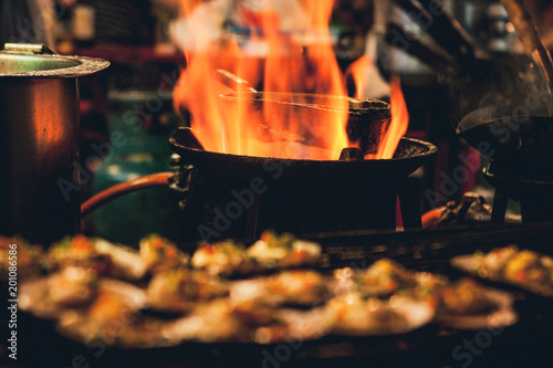 Canvas Print Grilled scallops sold at a street market stall with a pan covered with flames on the background