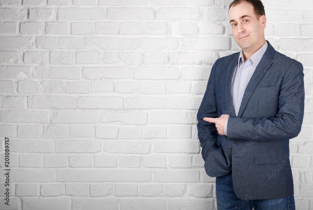 Positive looking mid age man in suit with pointing finger standing near white brick wall Positive looking mid age man in suit with pointing finger standing near white brick wall