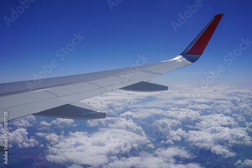 Part of the wing of a plane high in the blue sky among white clouds.