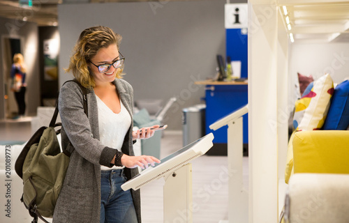Fotografie Woman with phone configuring furniture at the self-service device in the store
