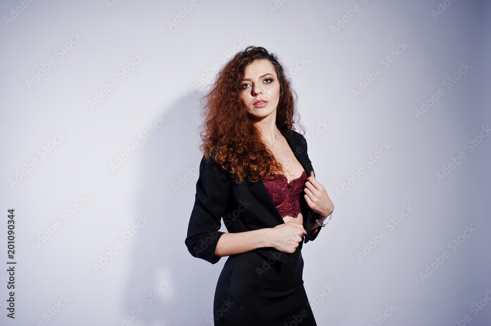Brunette curly haired girl in black office jacket with skirt, on bra at studio against white background. Sexy businesswoman. Brunette curly haired girl in black office jacket with skirt, on bra at studio against white background. Sexy businesswoman.