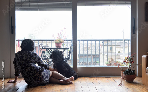 sad woman sitting and looking out the window with her dog